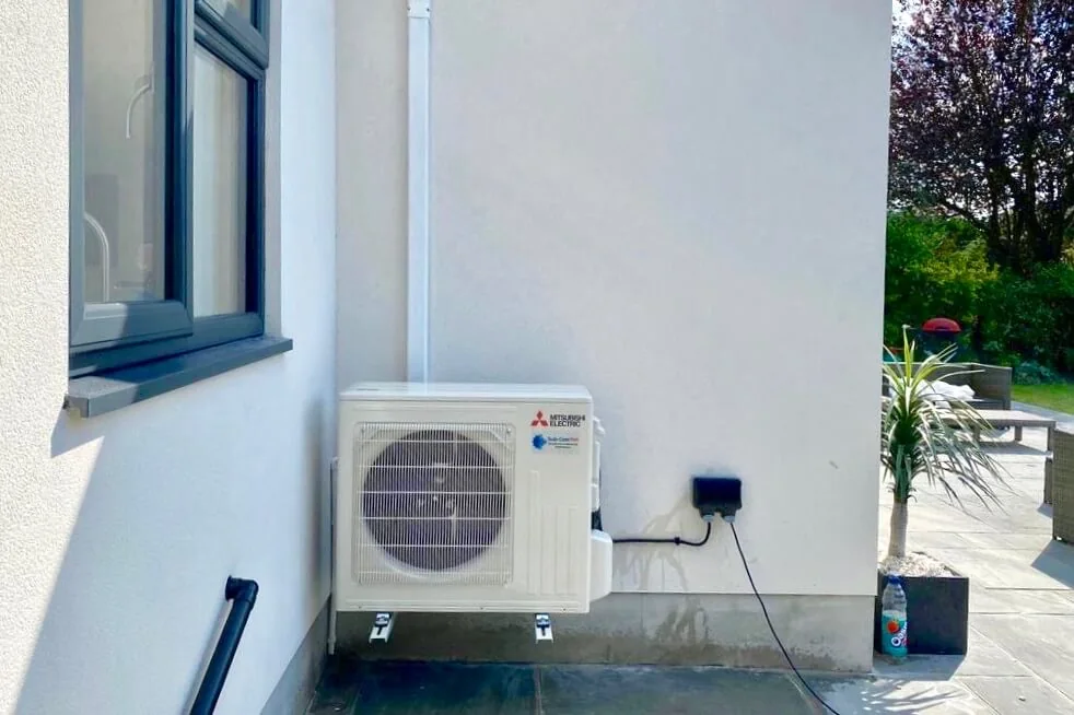 Mitsubishi Electric outdoor air-conditioning unit mounted beside a rendered house
