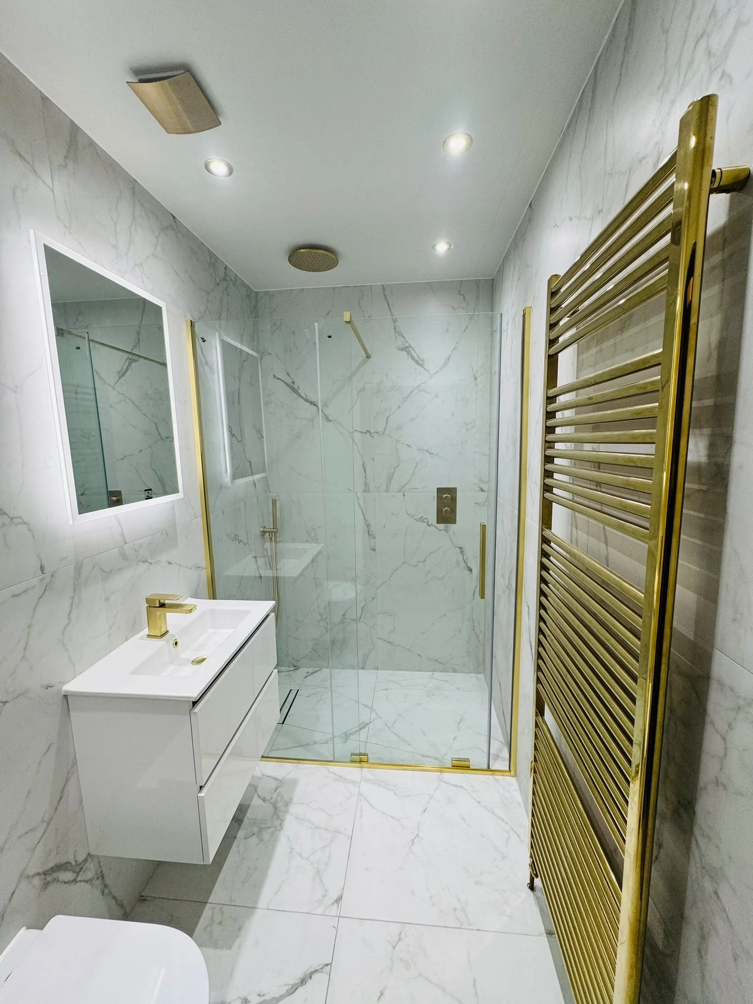 Completed marble-effect bathroom with gold shower enclosure, fittings and heated towel rail