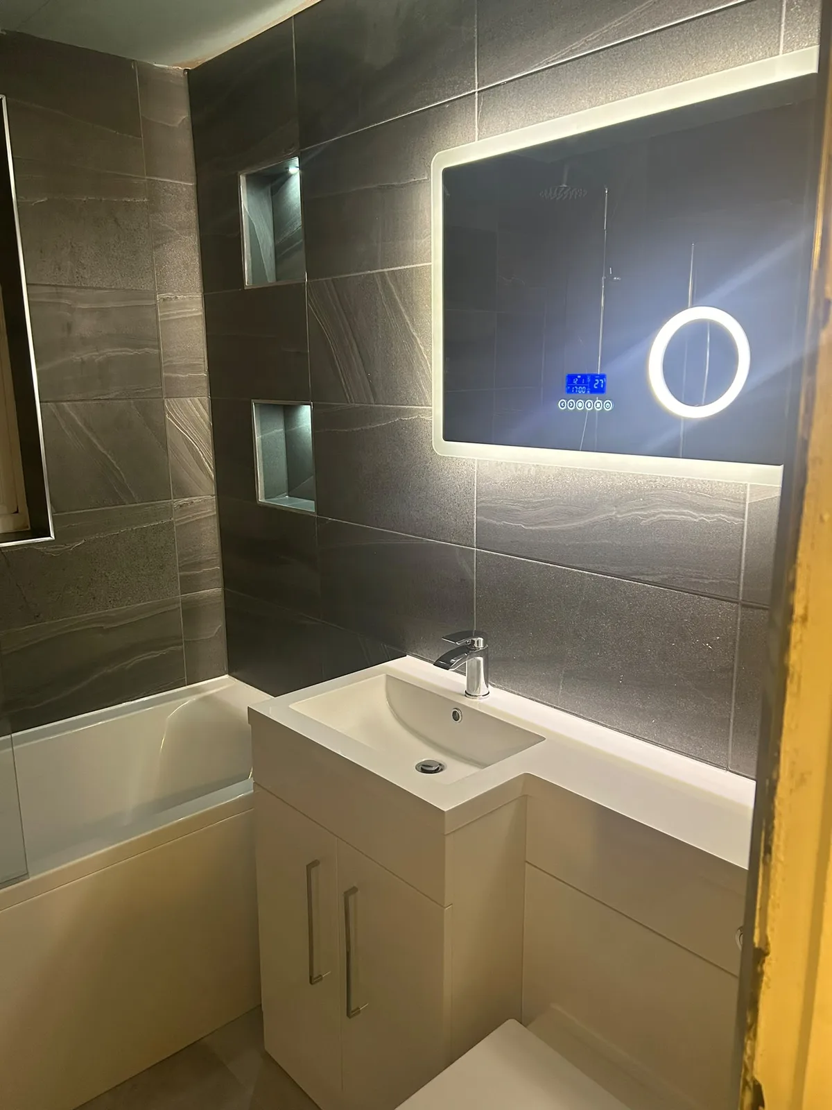 Contemporary dark tiled bathroom with illuminated mirror and vanity unit
