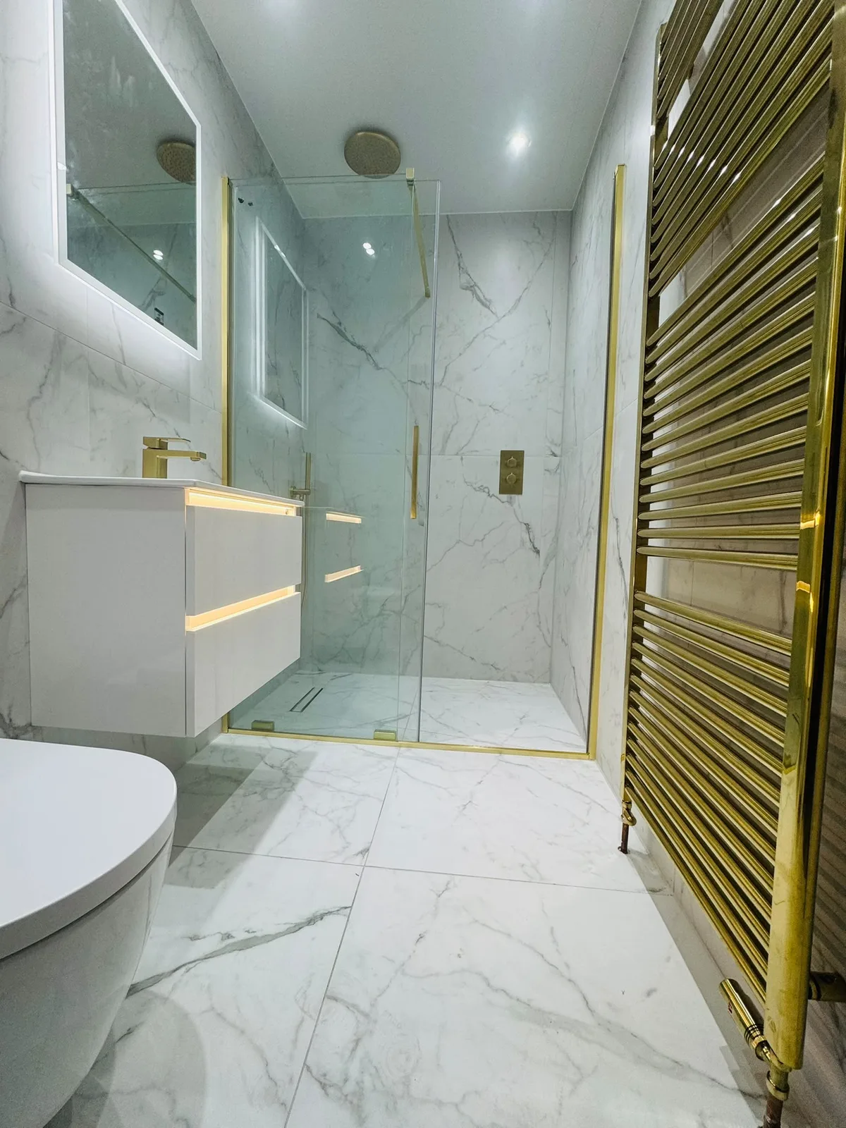 Completed walk-in shower bathroom with gold towel radiator and brass details