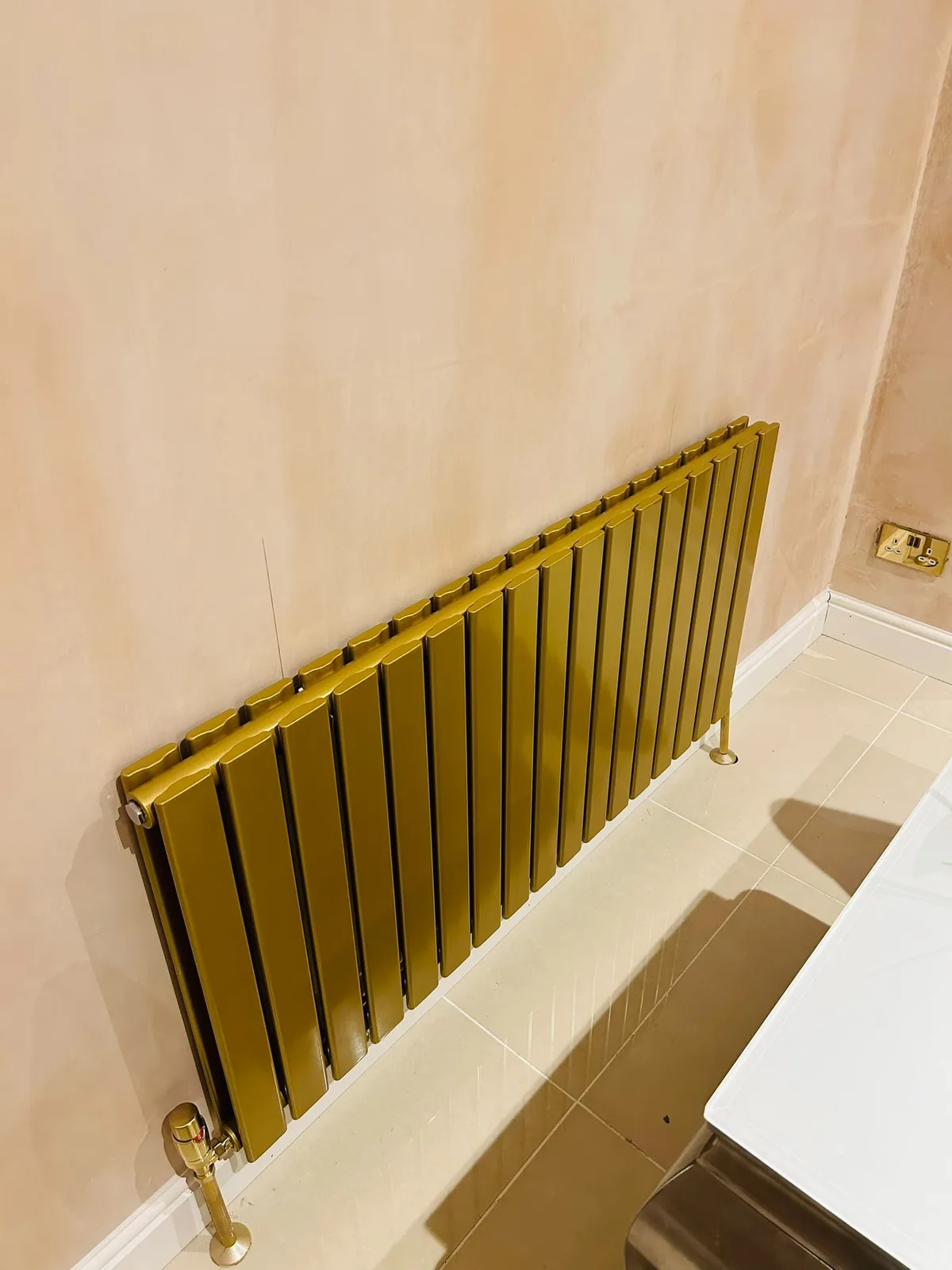Horizontal gold designer radiator installed against a finished wall