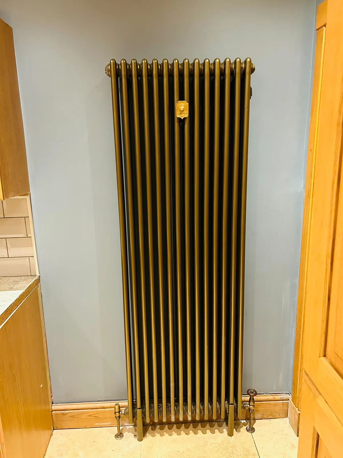 Tall vertical gold designer radiator installed in a kitchen area