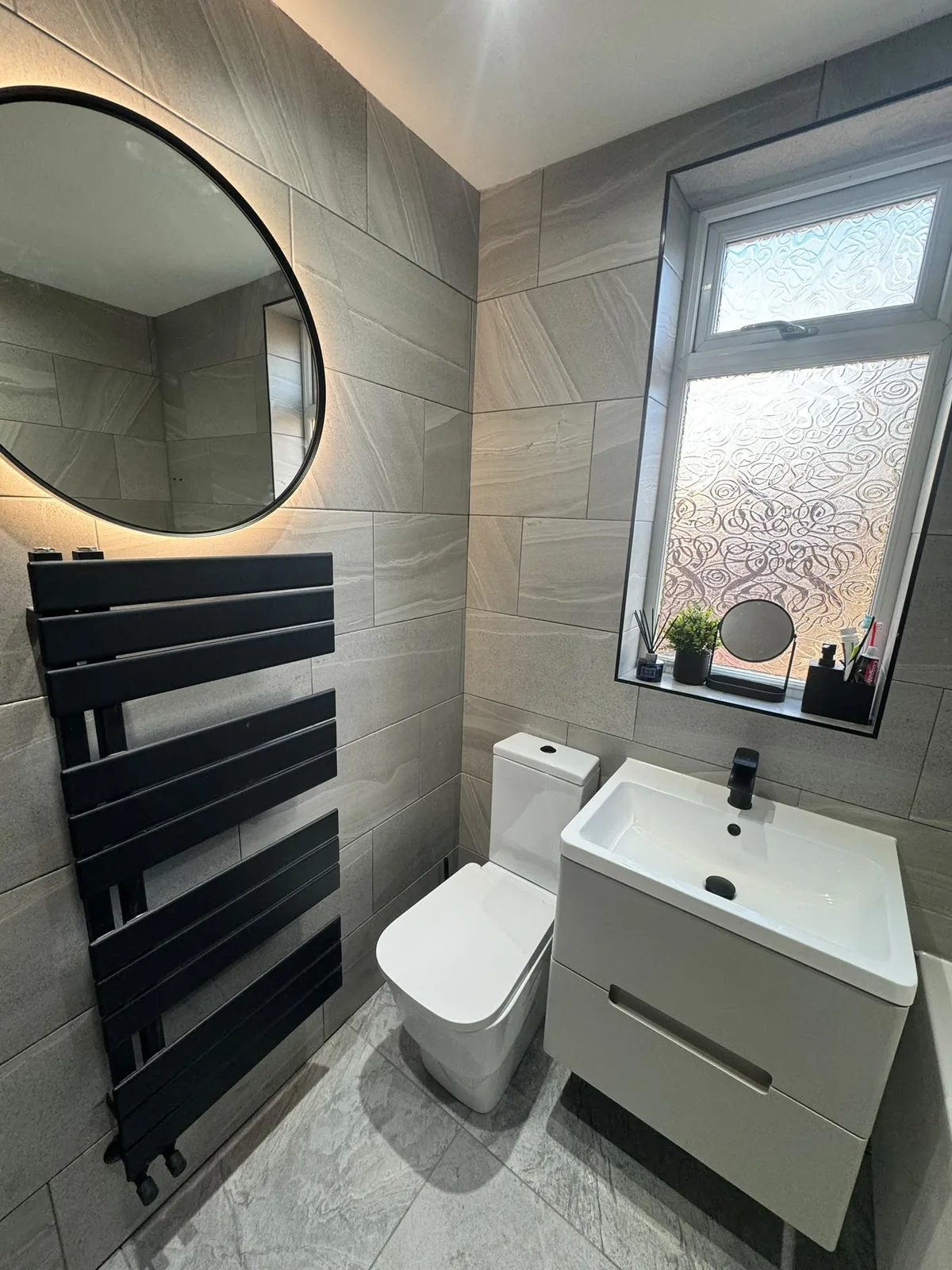Grey tiled bathroom with black fittings, toilet and vanity unit