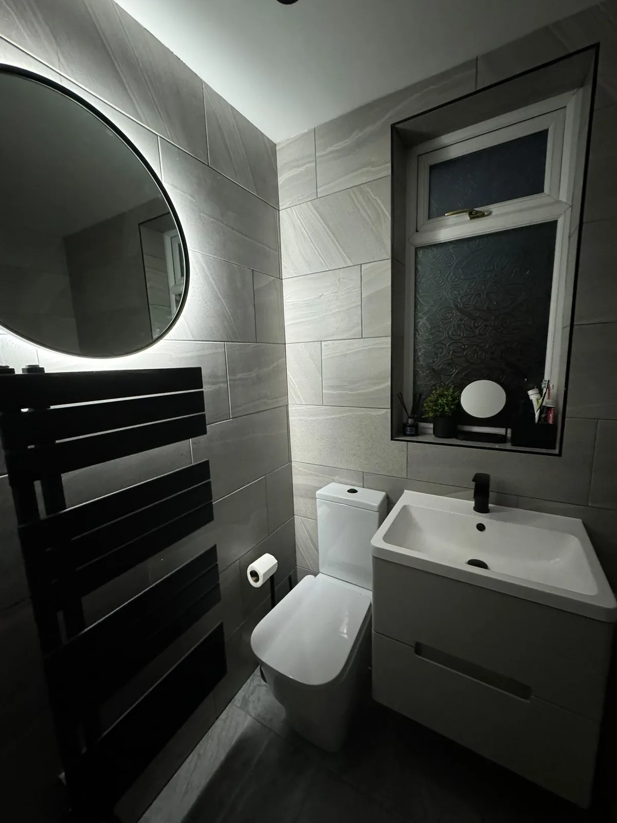 Grey tiled bathroom with black heated towel radiator and vanity basin