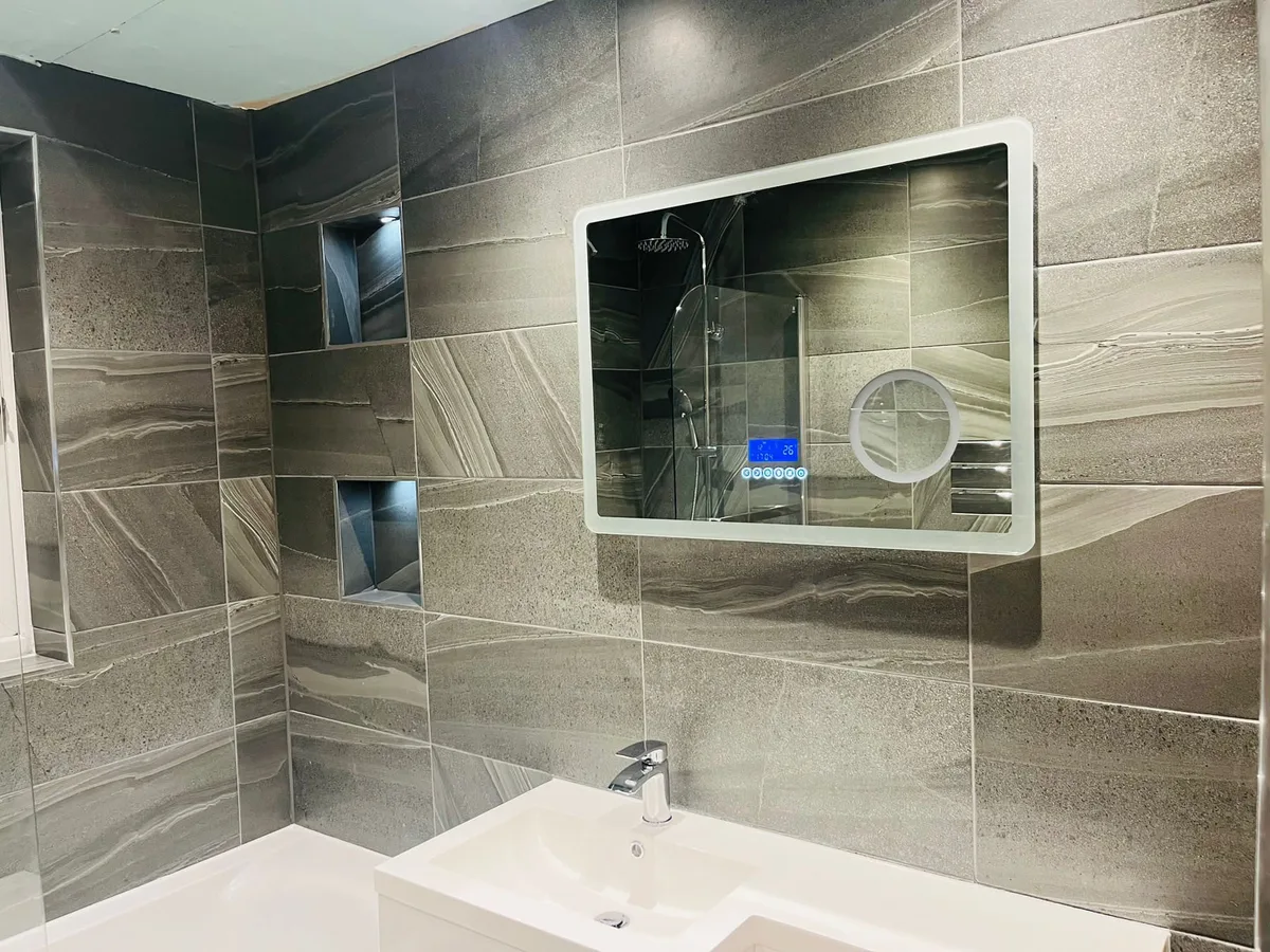 Completed grey tiled bathroom with illuminated mirror, bath and fitted vanity
