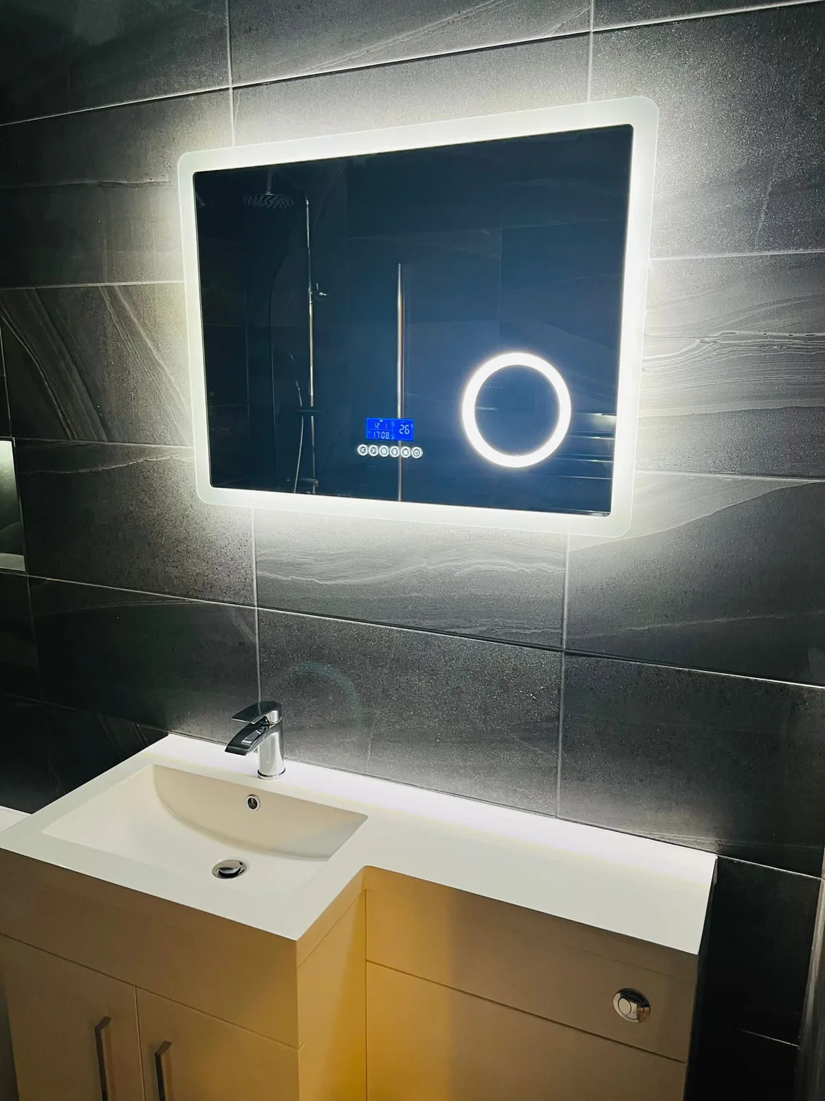 Illuminated bathroom mirror above a fitted basin and vanity unit
