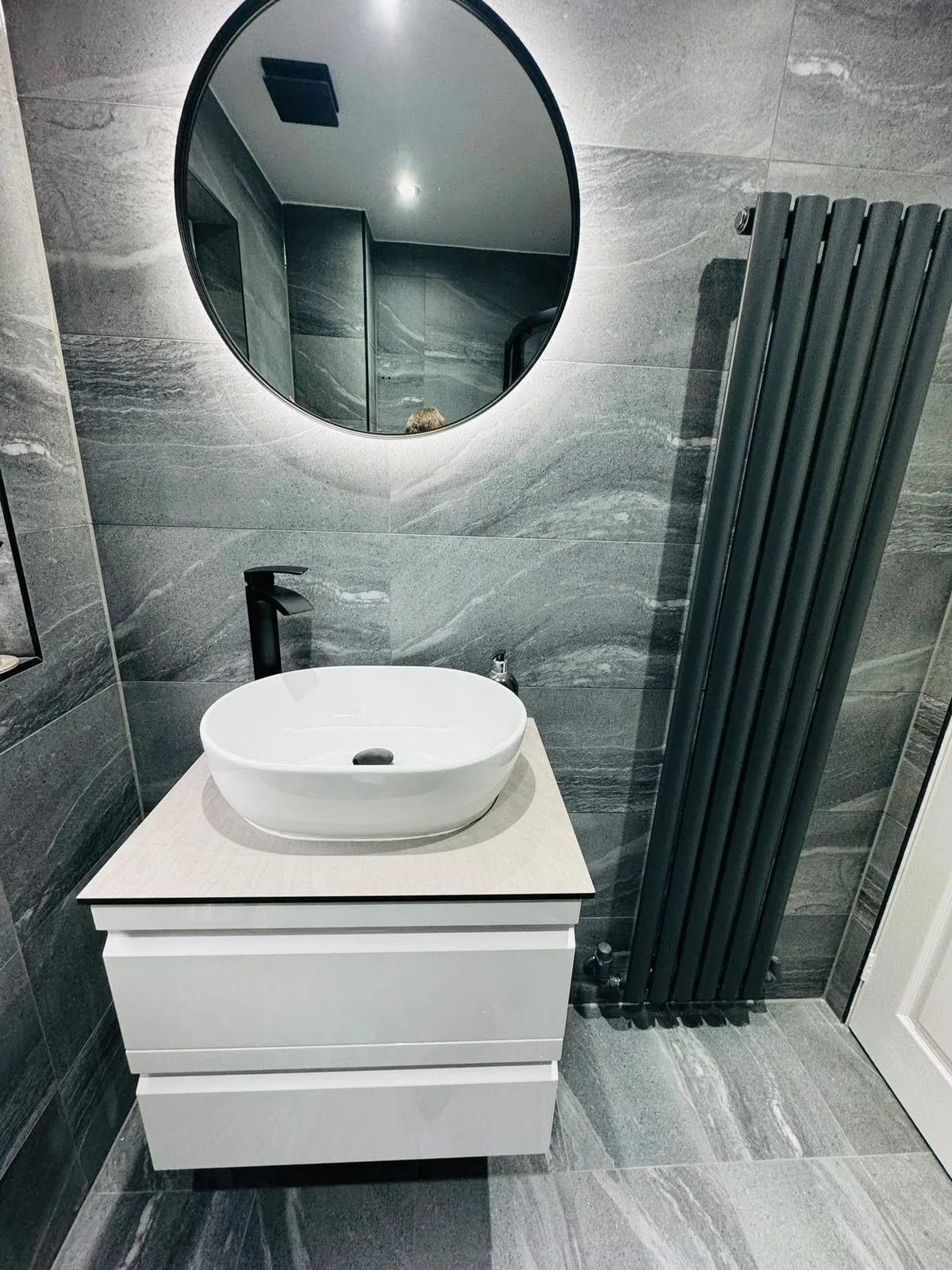 Grey tiled bathroom with countertop basin and tall black radiator